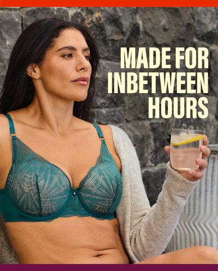 A woman wearing a teal lace underwire bra and a light gray cardigan, holding a glass of water with a lemon slice in front of a dark stone wall. The text 'MADE FOR INBETWEEN HOURS' is displayed on the right side.