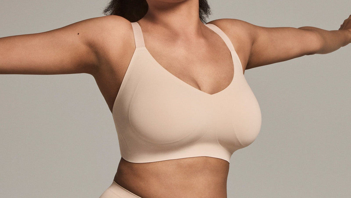 Woman wearing a nude colour wirefree bra set against a plain background