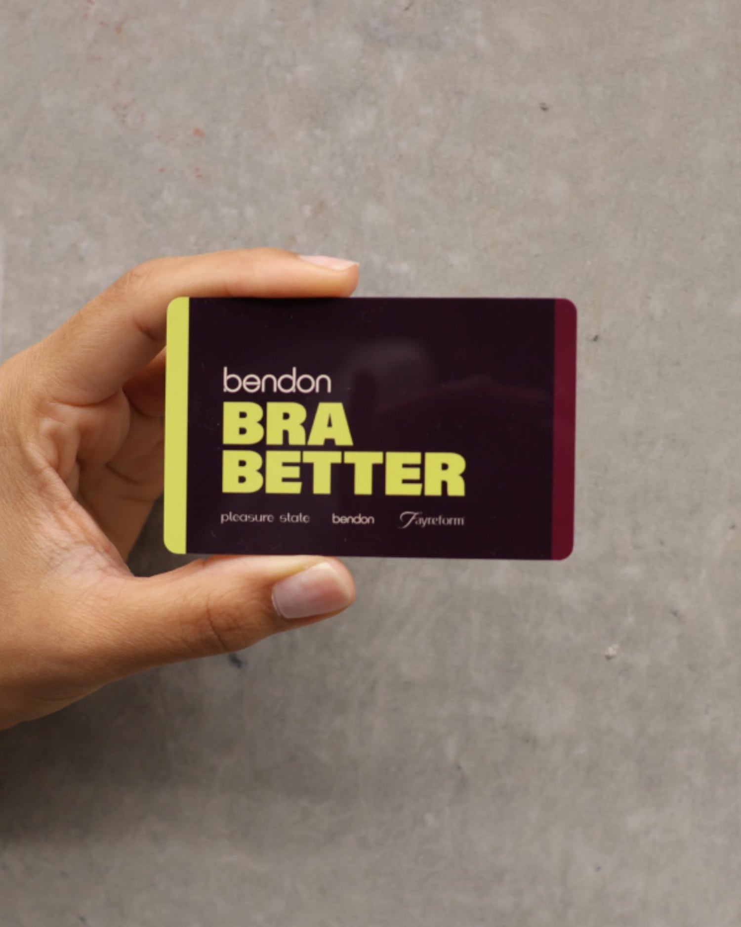 Hand holding a 'Bendon Bra Better' product packaging against a gray background