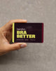 Hand holding a 'Bendon Bra Better' product packaging against a gray background
