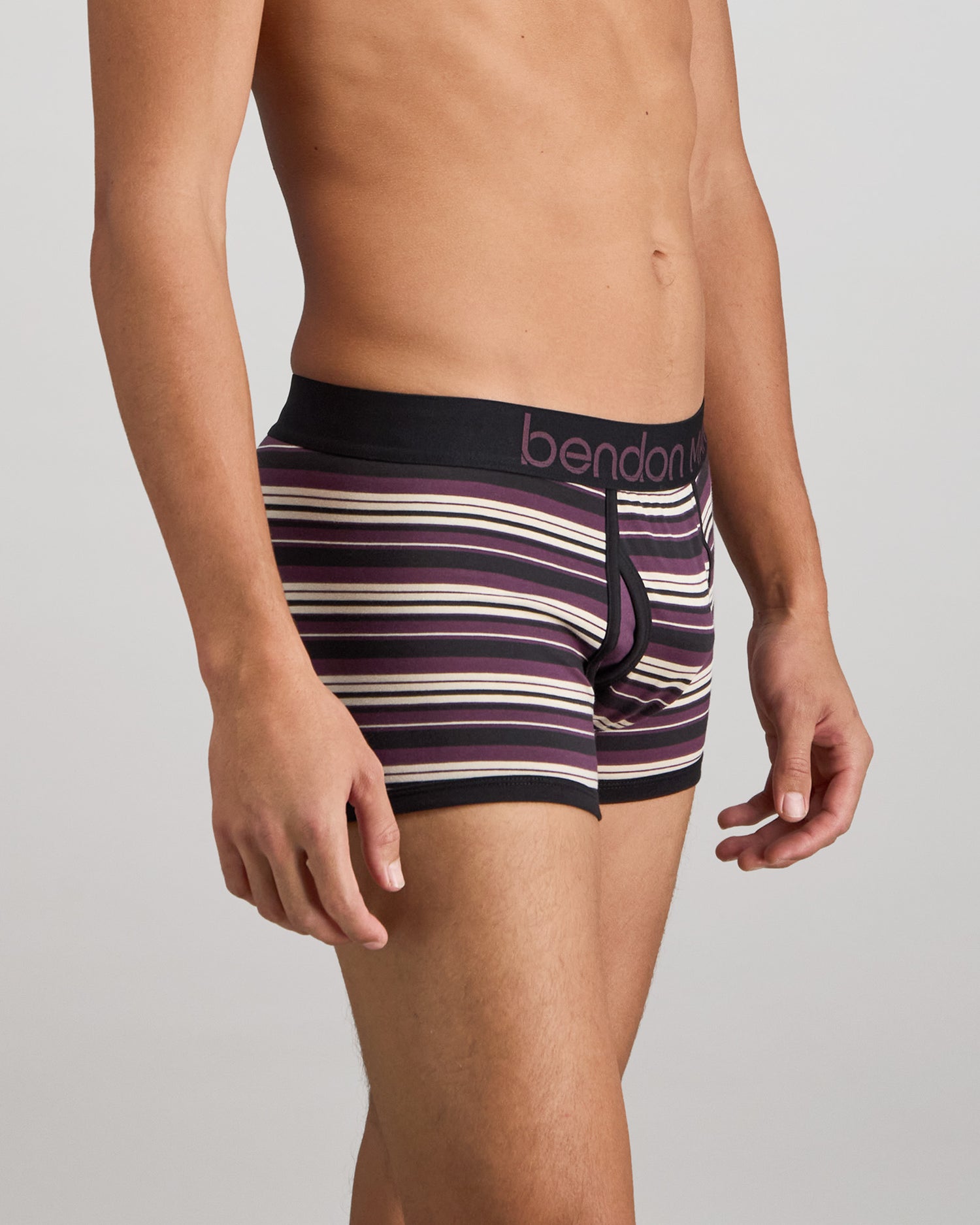 Model wears Bold Stripe Mens Trunk in BLACK/PLUM STRIPE. On body side view