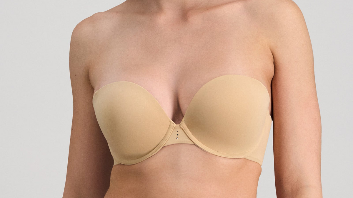 Beige strapless bra worn by a person on a plain background