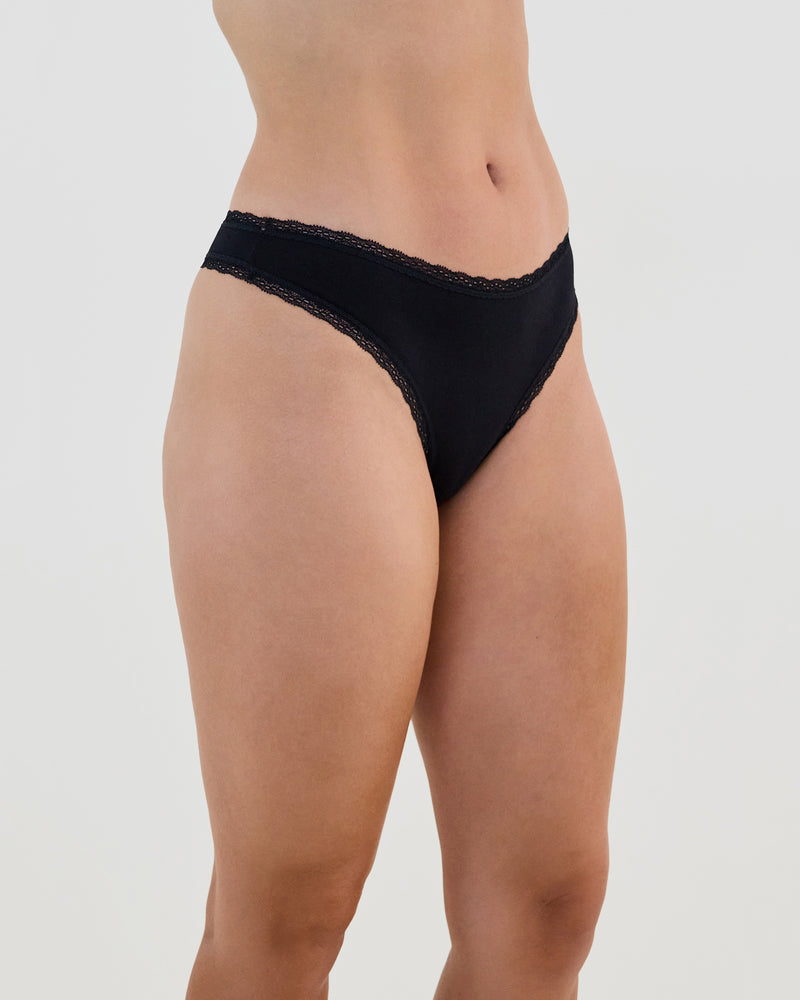 Model wears Stretch Cotton Thong in BLACK. On body side view