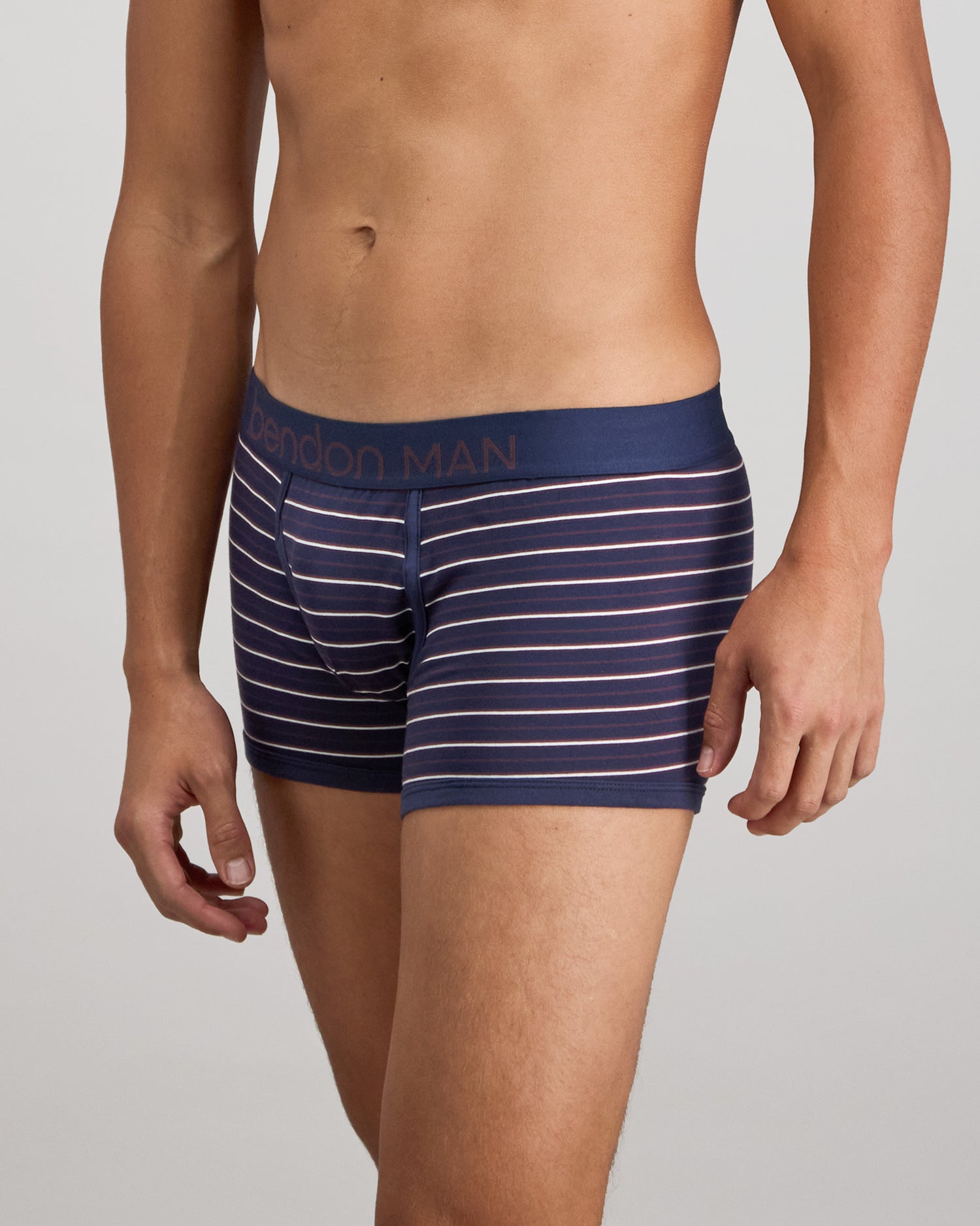 Model wears Bold Stripe Mens Trunk in PEACOAT/PLUM STRIPE. On body side view